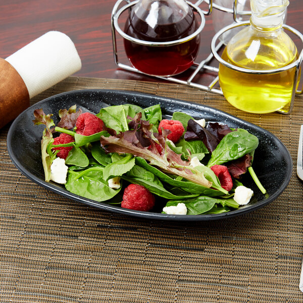 An Elite Global Solutions black deep oval melamine plate with a salad topped with raspberries and cheese.