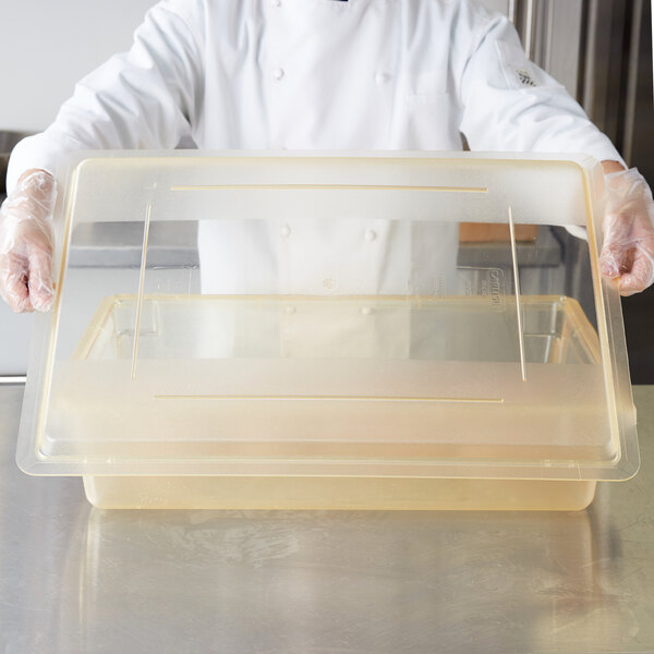 A chef in a white coat placing a yellow Carlisle StorPlus lid on a plastic food storage container on a counter.