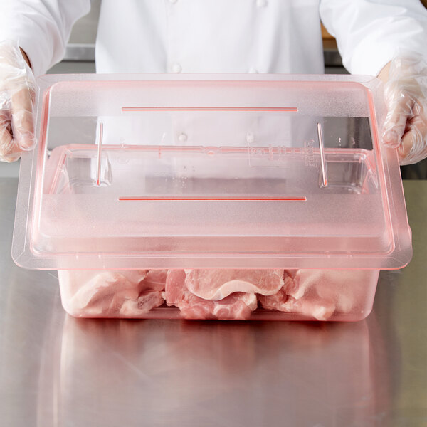 A person in a white coat placing raw meat in a Carlisle StorPlus red plastic container.