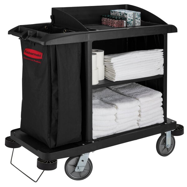 A Rubbermaid housekeeping cart with a shelf full of white folded towels and a bag.