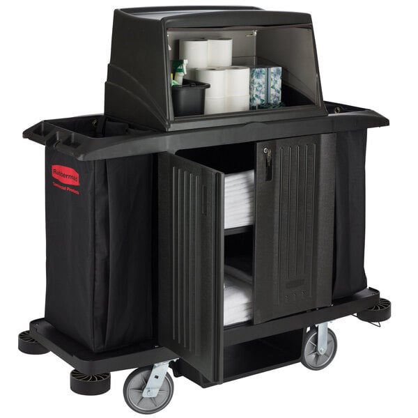 A black Rubbermaid housekeeping cart with a shelf full of towels and a large black bag.