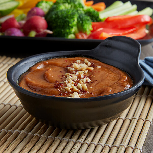 A black Elite Global Solutions melamine sauce bowl filled with food and nuts.