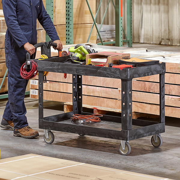 A man using a black Rubbermaid utility cart with tools on it.