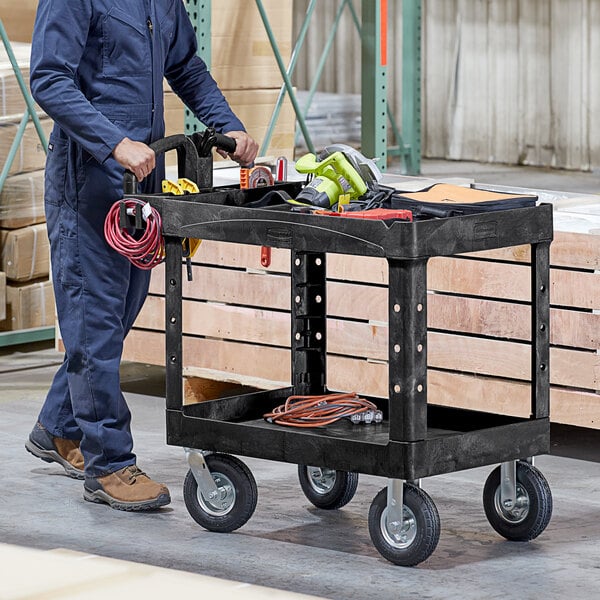 A man pushing a Rubbermaid utility cart with tools.
