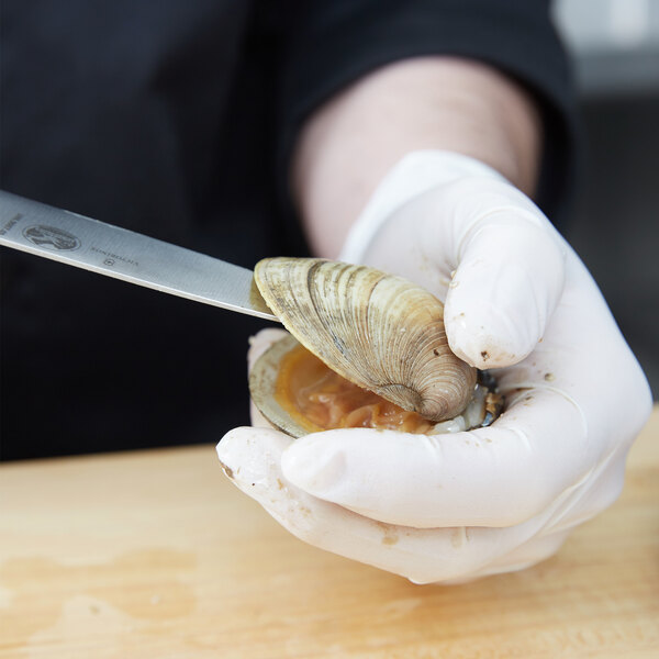 A gloved hand uses a Victorinox clam knife to cut a clam shell.