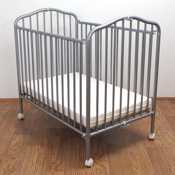 A L.A. Baby pewter colored metal folding crib with a mattress on it.
