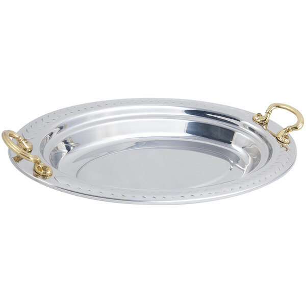 A stainless steel oval food pan with a laurel design and round brass handles.