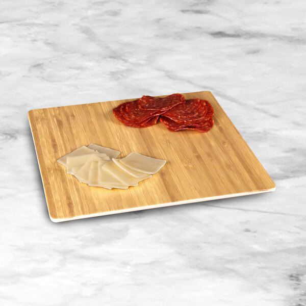 An Elite Global Solutions faux bamboo melamine serving board with slices of meat and cheese on it.