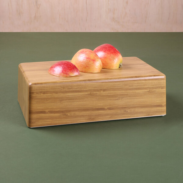 A rectangular faux bamboo modular riser with apples on top of it.