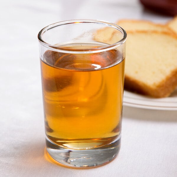 An Anchor Hocking Regency glass cup filled with brown liquid next to a plate of bread.