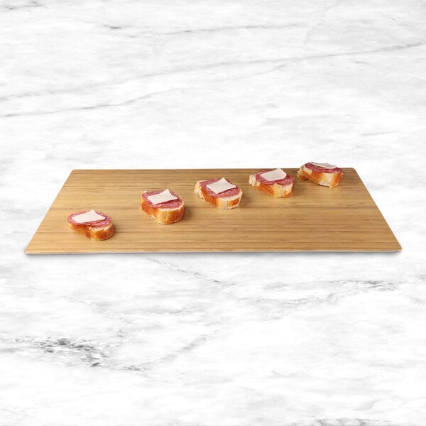 A rectangular faux bamboo melamine serving board with sandwiches, cheese, and bread on it.