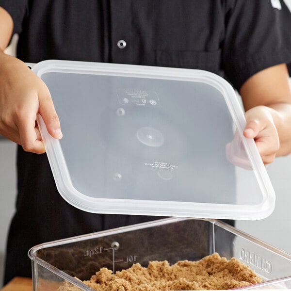 A person placing a translucent plastic lid on a Cambro square food storage container.