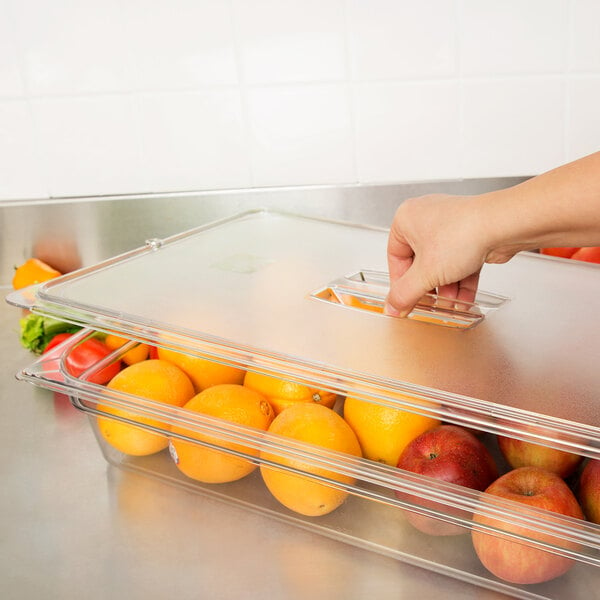 A hand reaching for a plastic container of oranges and apples.