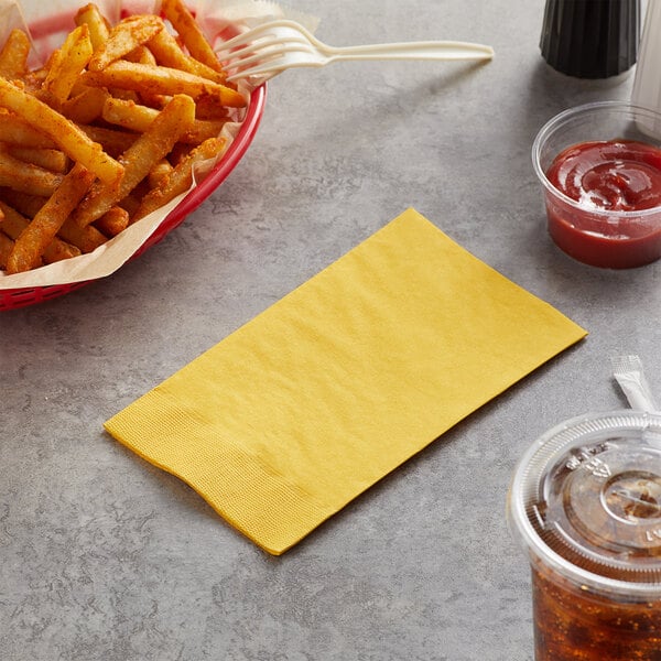 A bowl of french fries with a yellow napkin on a table with a container of ketchup.