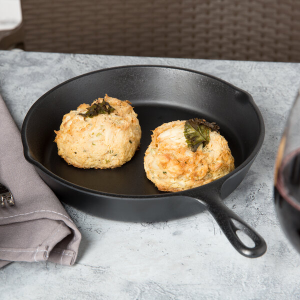 Black faux cast iron Elite Global Solutions fry pan with two scones and food next to a glass of wine.