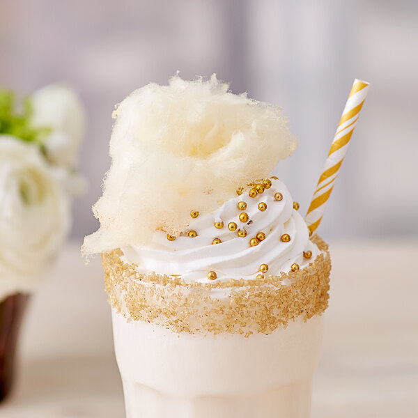 A milkshake with a straw and cotton candy on top of white and gold frosting.