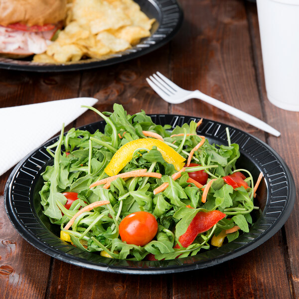 A Dart foam plate with salad and a fork on a table.