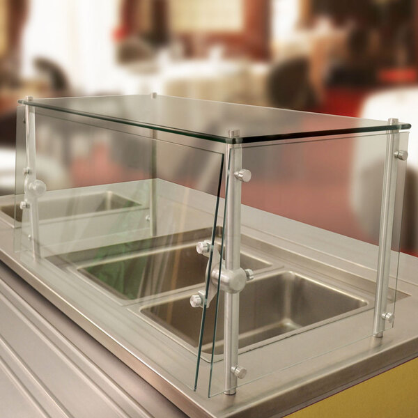 A stainless steel cafeteria food shield with a glass top over a counter.