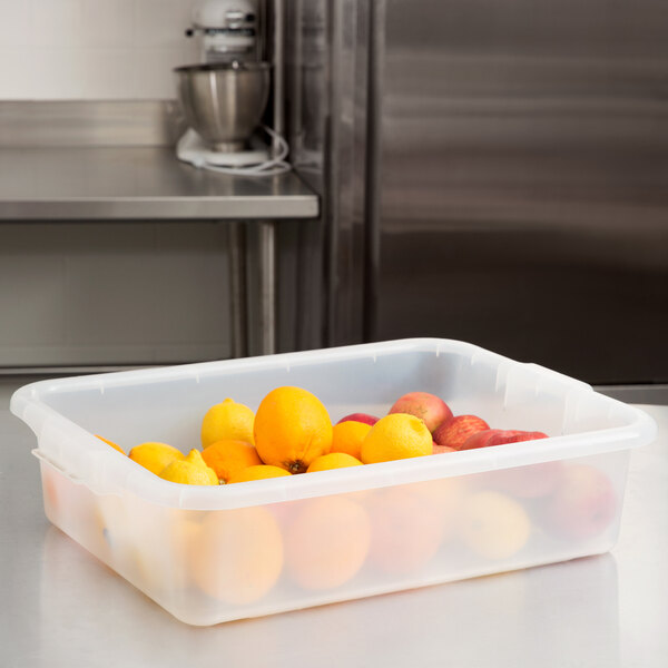 A Vollrath Traex Color-Mate clear plastic container of oranges on a counter.