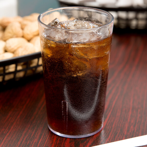 A Cambro clear plastic tumbler filled with ice tea on a table with a bowl of peanuts.