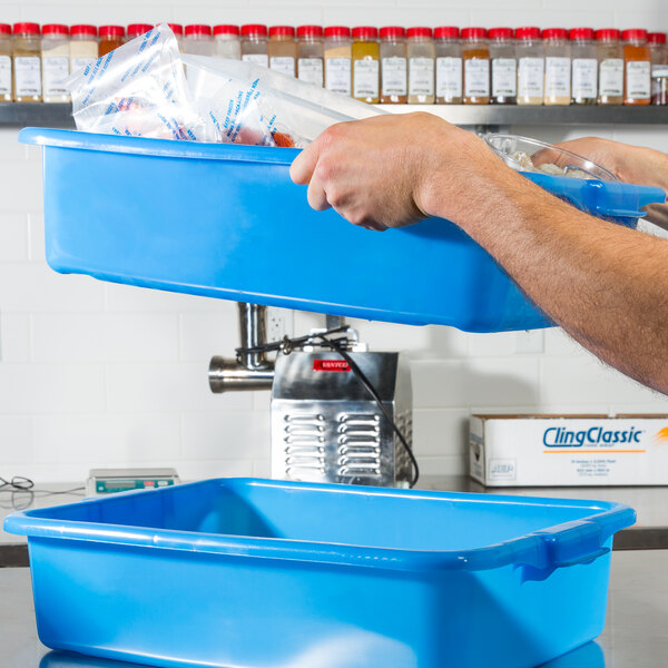 A man holding a Vollrath Traex blue perforated drain box on a counter.