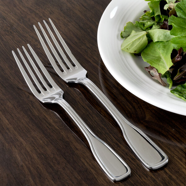 A Oneida Stanford stainless steel dinner fork next to a plate of salad on a table.