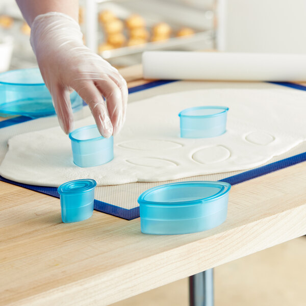 A person's gloved hand using a blue plastic football cutter to cut dough.