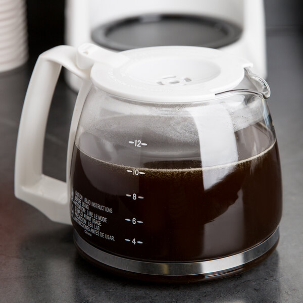 A Proctor Silex coffee carafe with a white handle full of coffee sitting on a counter.