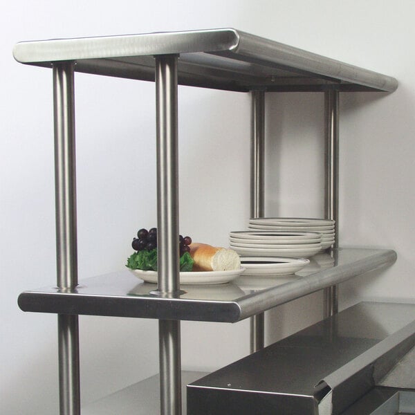A stainless steel Advance Tabco double deck overshelf on a counter with plates and food on it.