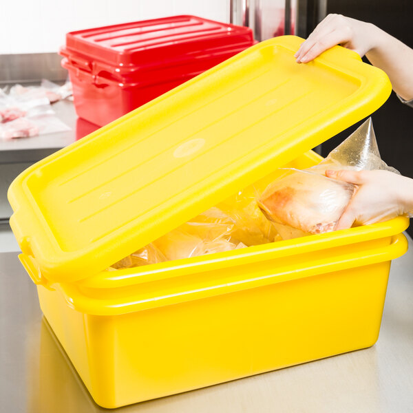 A woman using a yellow Vollrath Traex food storage container with a plastic lid to store food.