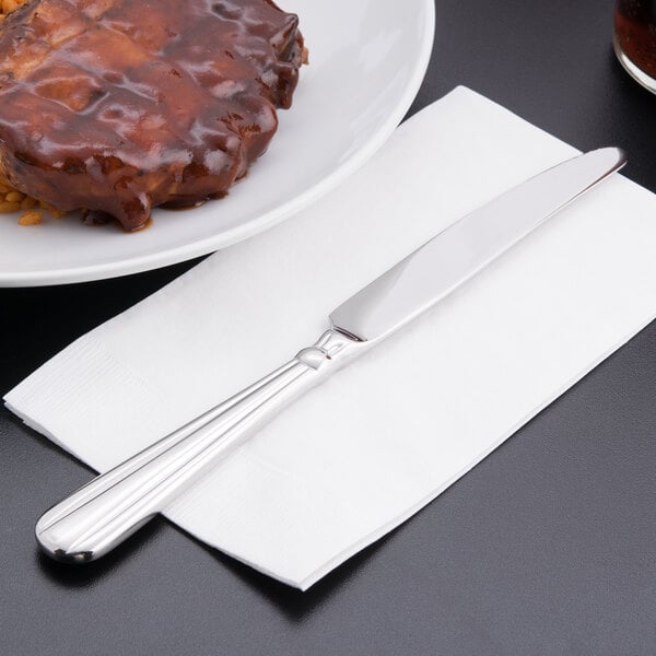A plate of meat with a Oneida Unity stainless steel dinner knife on a napkin.