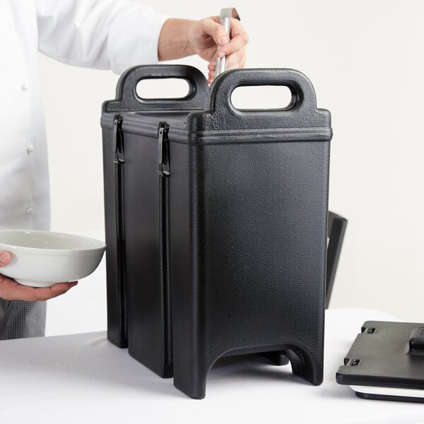 A chef using a Cambro black insulated soup carrier to hold a bowl of food.