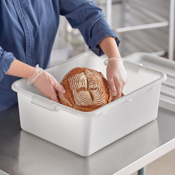 A person in gloves holding a loaf of bread in a white polypropylene container.