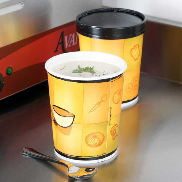 Two Huhtamaki paper soup cups with lids filled with soup on a counter with a spoon.