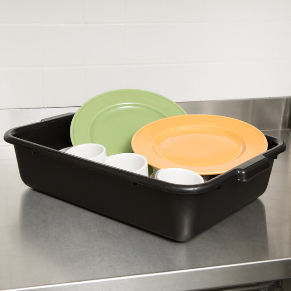 A black Tablecraft plastic bus tub on a stainless steel counter with plates and cups.