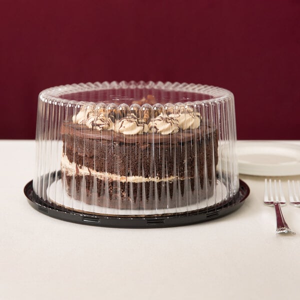 A chocolate cake in a D&W Fine Pack plastic cake container with a clear dome lid on a table in a bakery display.