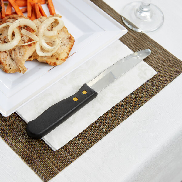 An American Metalcraft stainless steel steak knife with a plastic handle on a napkin next to a plate of food.