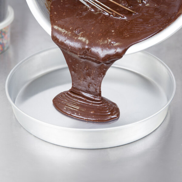 A person stirring chocolate sauce in a Vollrath round aluminum cake pan.