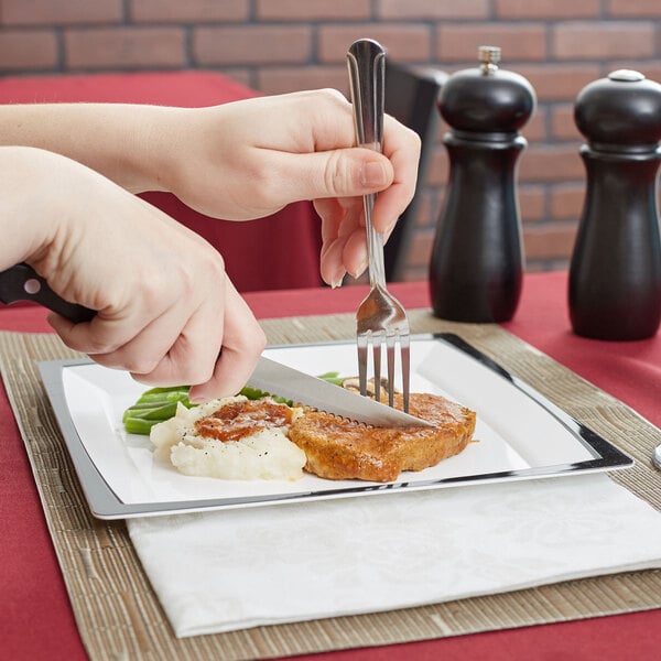 A person cutting a piece of meat with an American Metalcraft stainless steel steak knife with a black POM handle.
