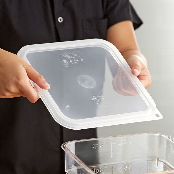 A person holding a Cambro CamSquares translucent square polypropylene food storage container with a lid.