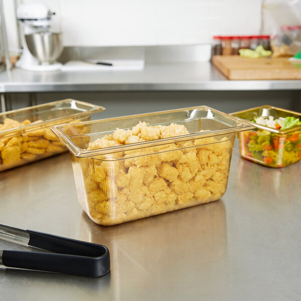 A Vollrath amber plastic food pan filled with food on a counter.