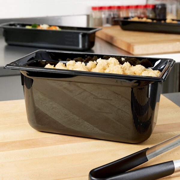 A close-up of a black Vollrath plastic food pan with food in it.