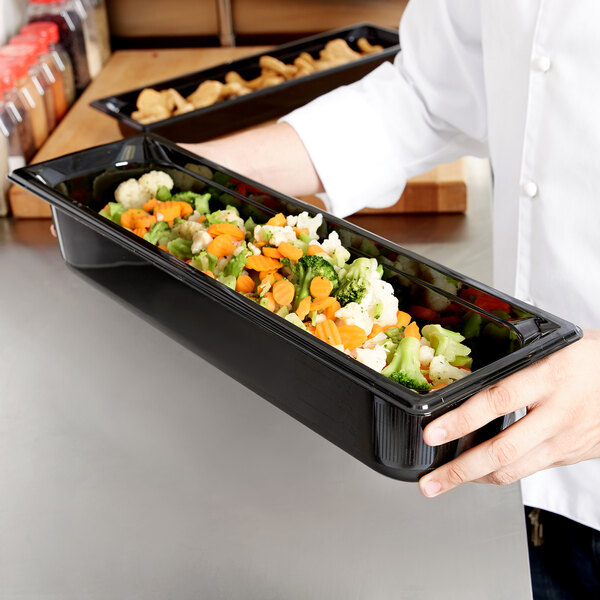 A chef holding a Vollrath black plastic food pan filled with vegetables.