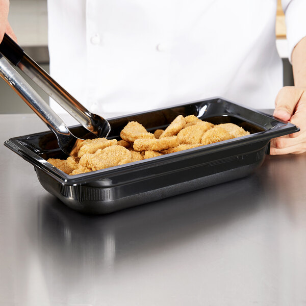 A chef using a spatula to serve food in a black Vollrath plastic food pan.