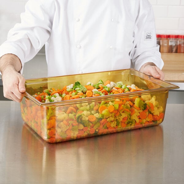 A chef holding a Vollrath amber plastic food pan full of vegetables.
