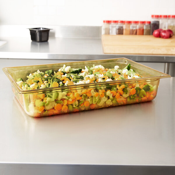 A Vollrath amber plastic food pan filled with vegetables on a counter.
