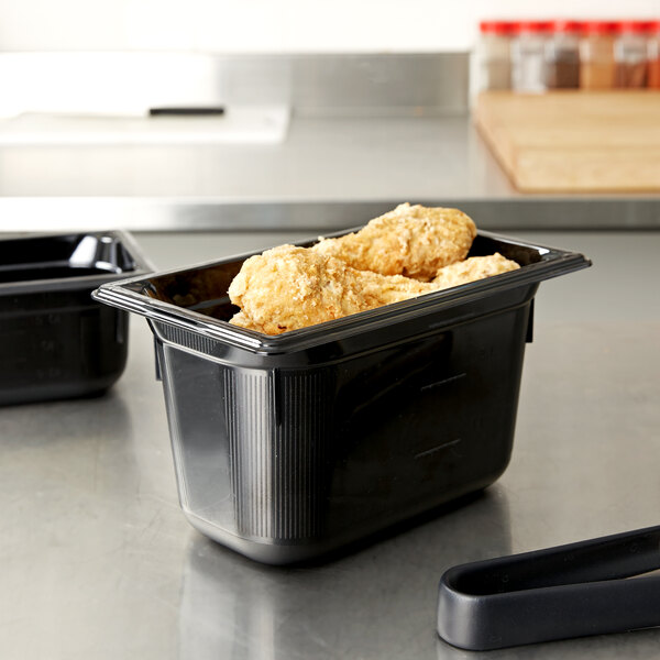 A black Vollrath Super Pan plastic food pan with food in it on a counter.