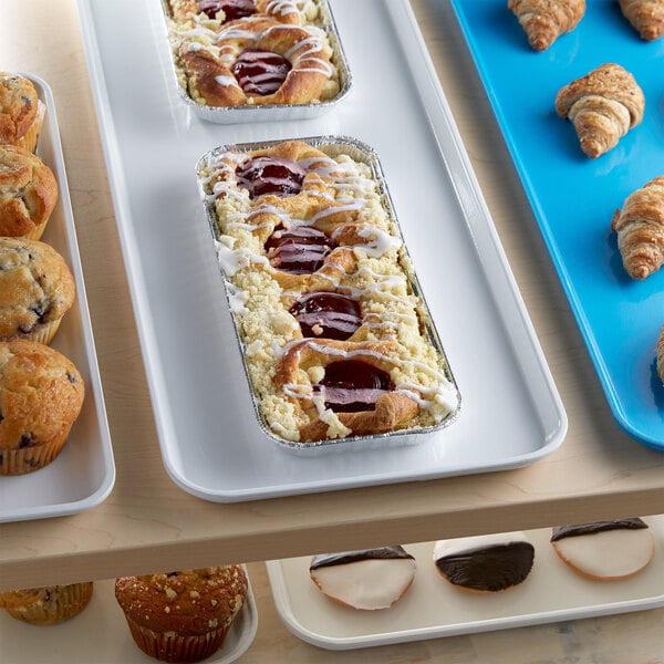 A white Cambro market tray of pastries and muffins on a bakery display counter.
