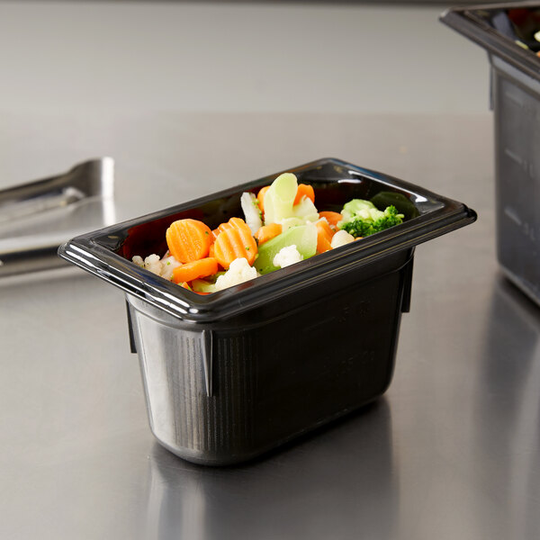 A black Vollrath plastic food pan with vegetables inside on a counter.