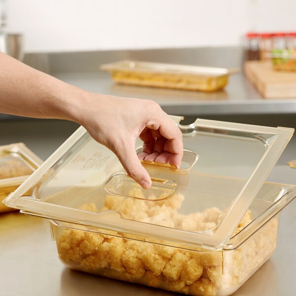 A hand placing a Vollrath Amber High Heat Slotted Cover on a plastic container of food.